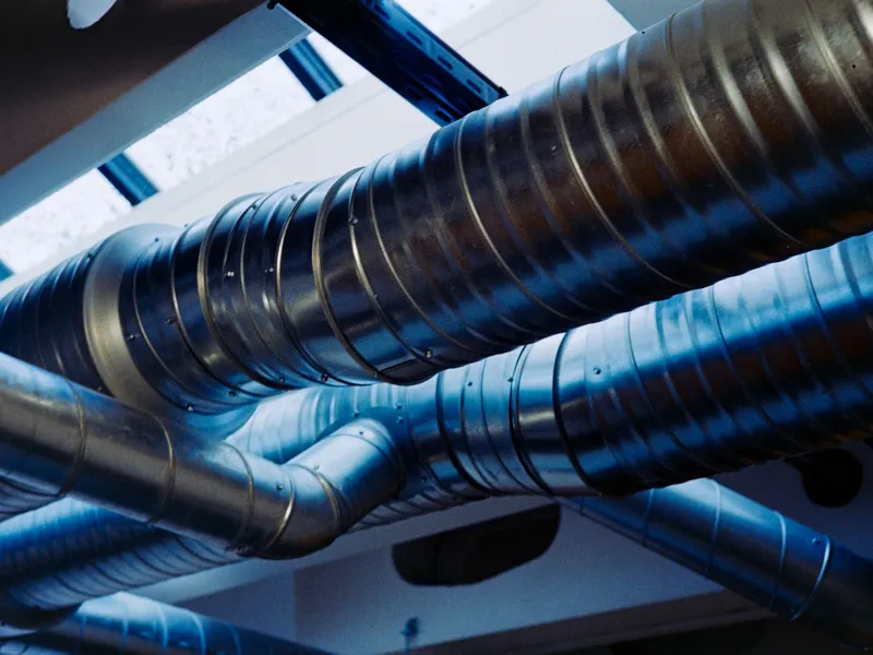 Spiral steel ductwork and insulated HVAC lines running along a ceiling